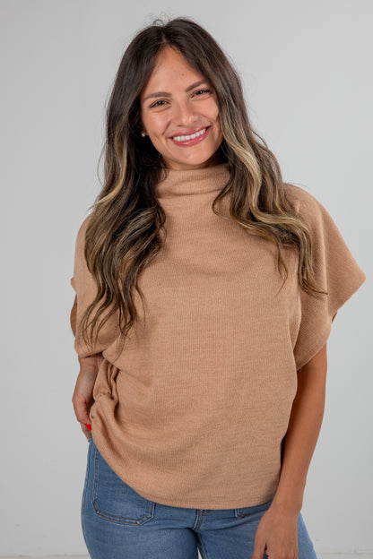 Woman wearing a brown turtleneck sweater and blue jeans against a plain background
