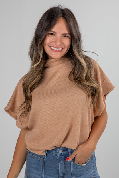 Woman wearing a tan sweater and blue jeans against a gray background