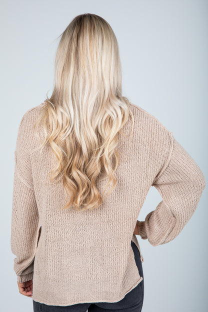 Person wearing a beige sweater with long blonde hair on a light gray background