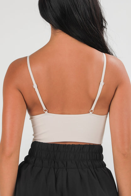 Person wearing a beige tank top with thin straps on a plain background