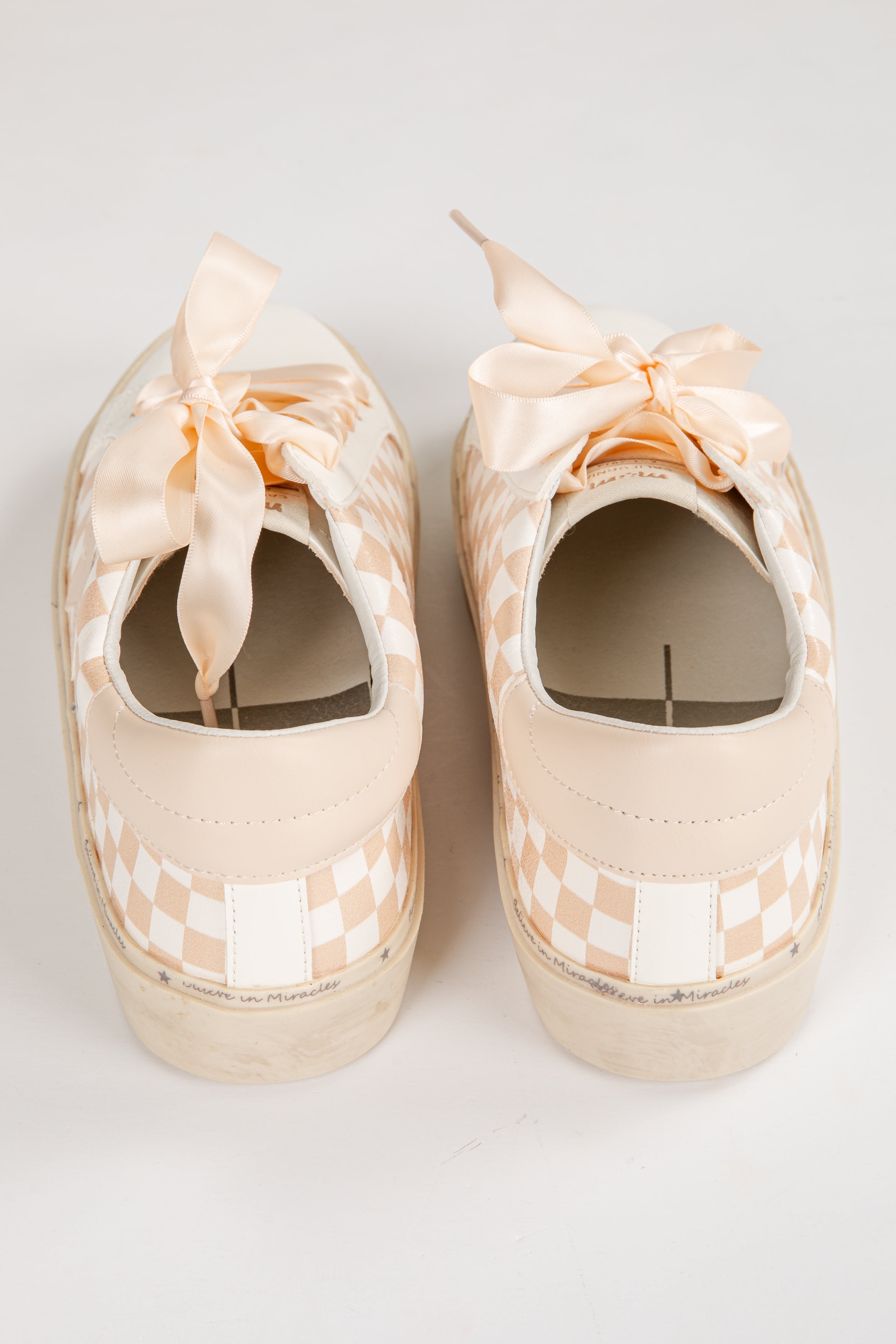Pair of beige checkered shoes with ribbons on a white background
