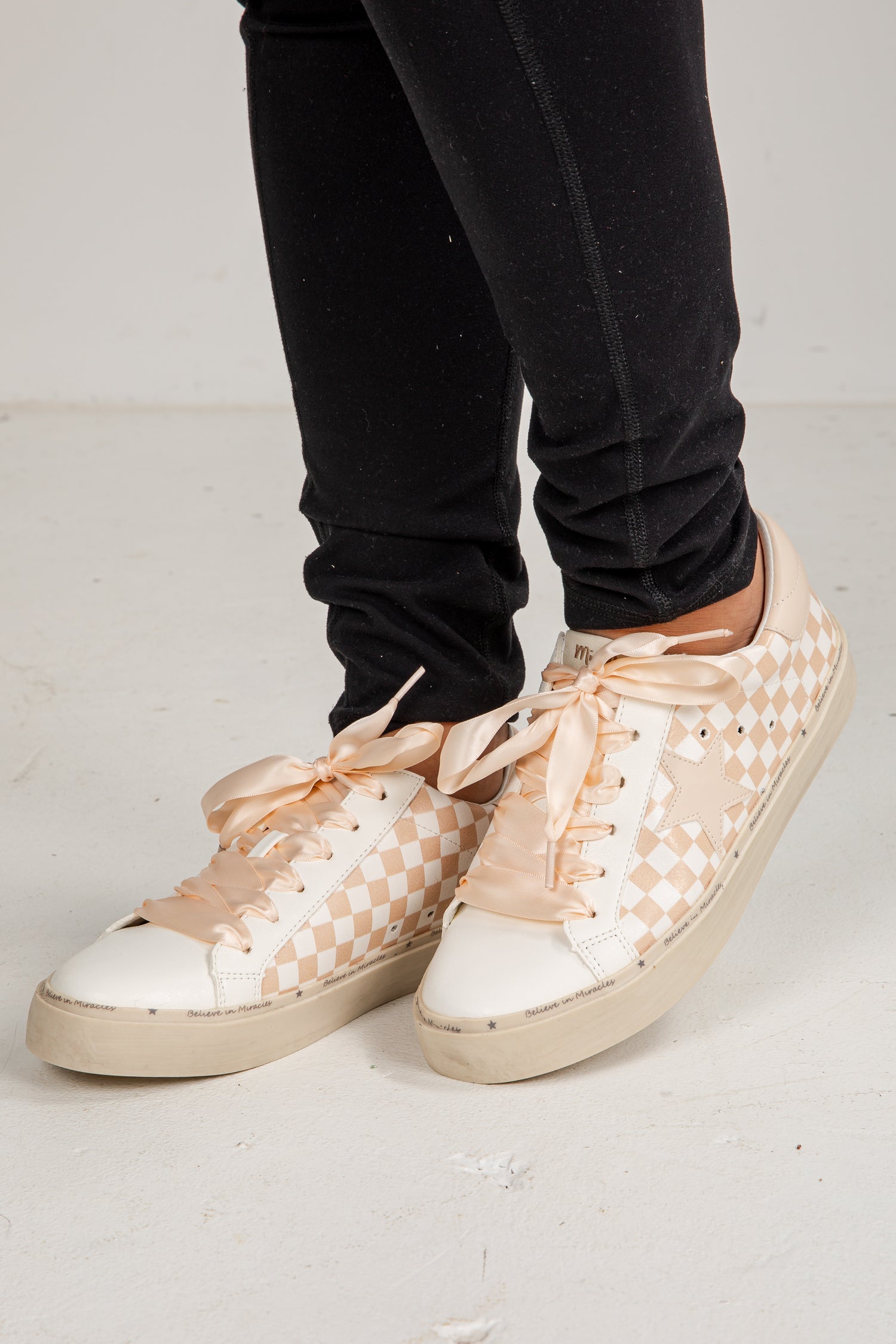 Beige checkered sneakers worn with black pants on a light gray background