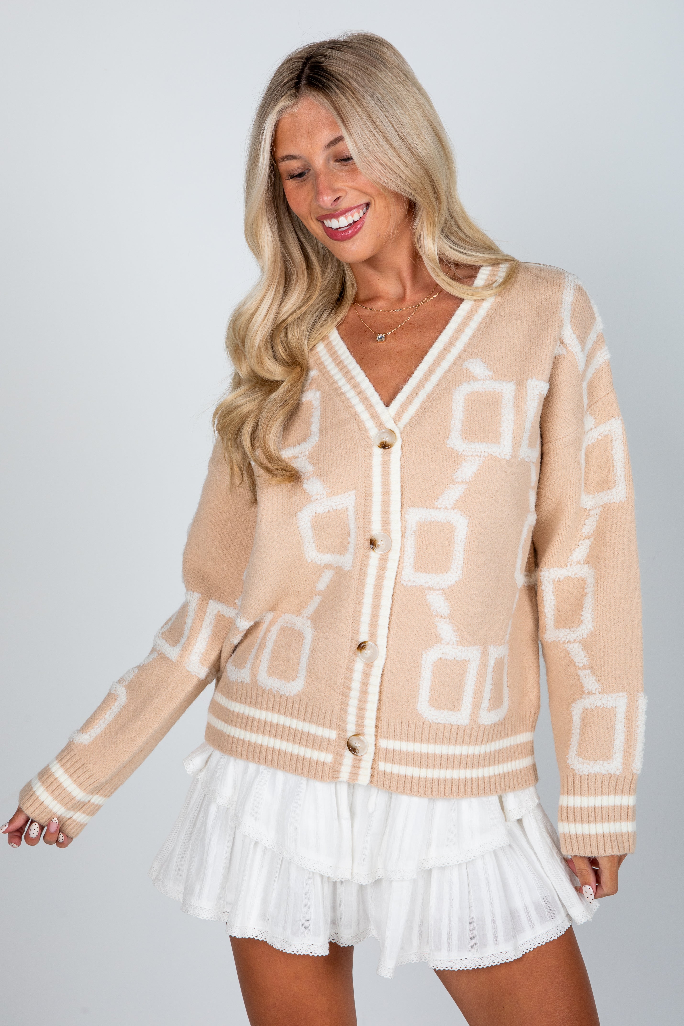 Woman wearing a beige patterned cardigan over a white dress on a plain background
