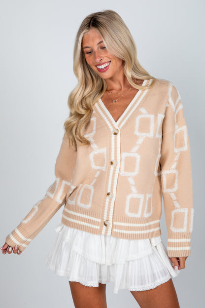 Woman wearing a beige patterned cardigan over a white dress on a plain background