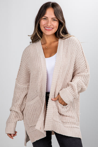 Woman wearing a beige chunky knit cardigan on a plain background