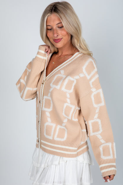 Woman wearing a beige sweater with geometric pattern on a plain background