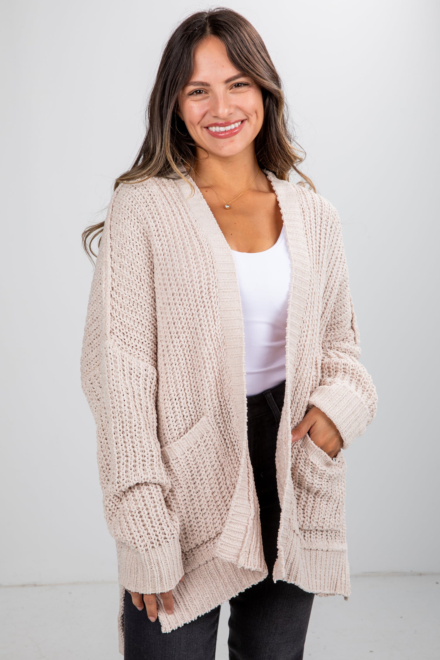 Woman wearing a beige knitted cardigan over a white top and black pants on a white background