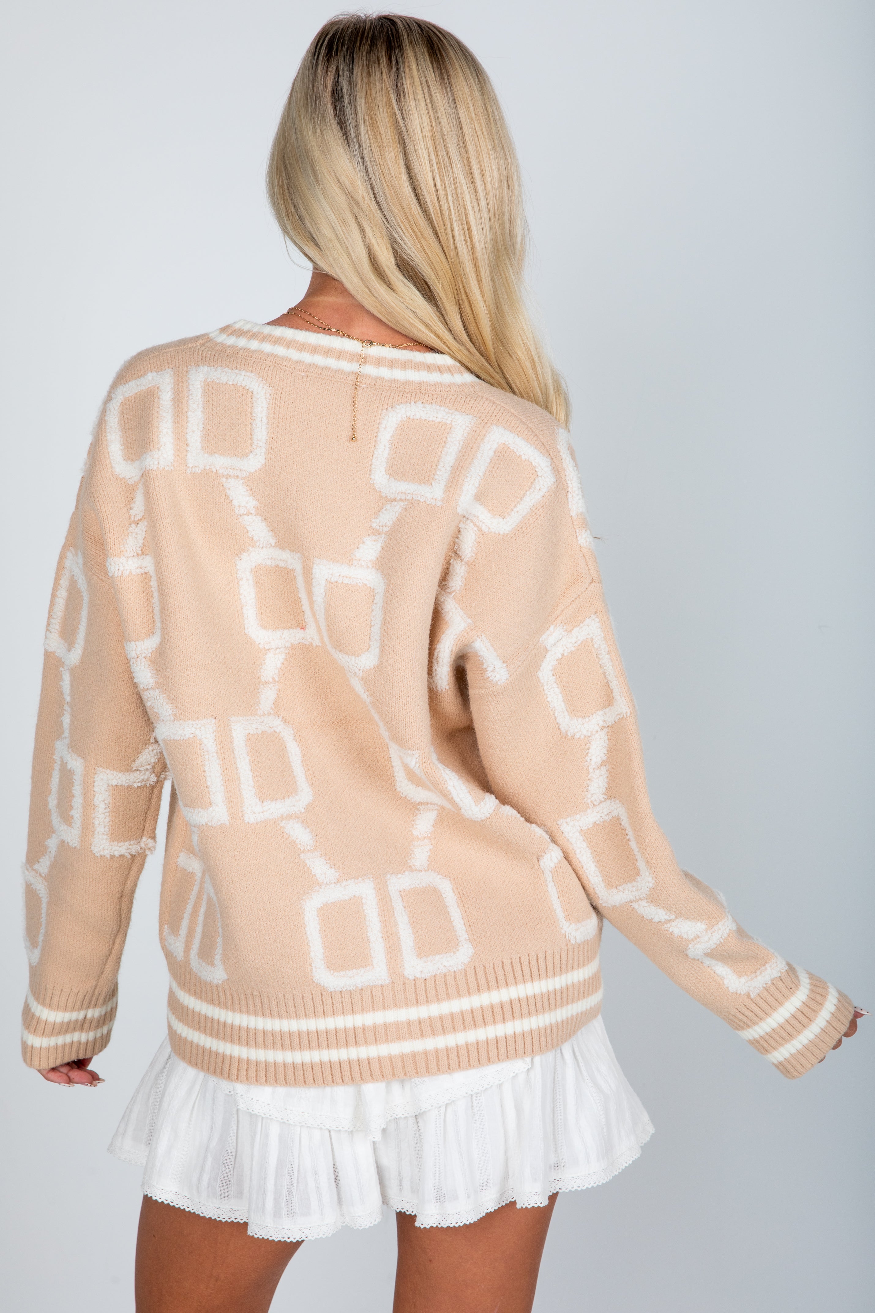 Woman wearing a beige sweater with geometric patterns and a white skirt on a light gray background