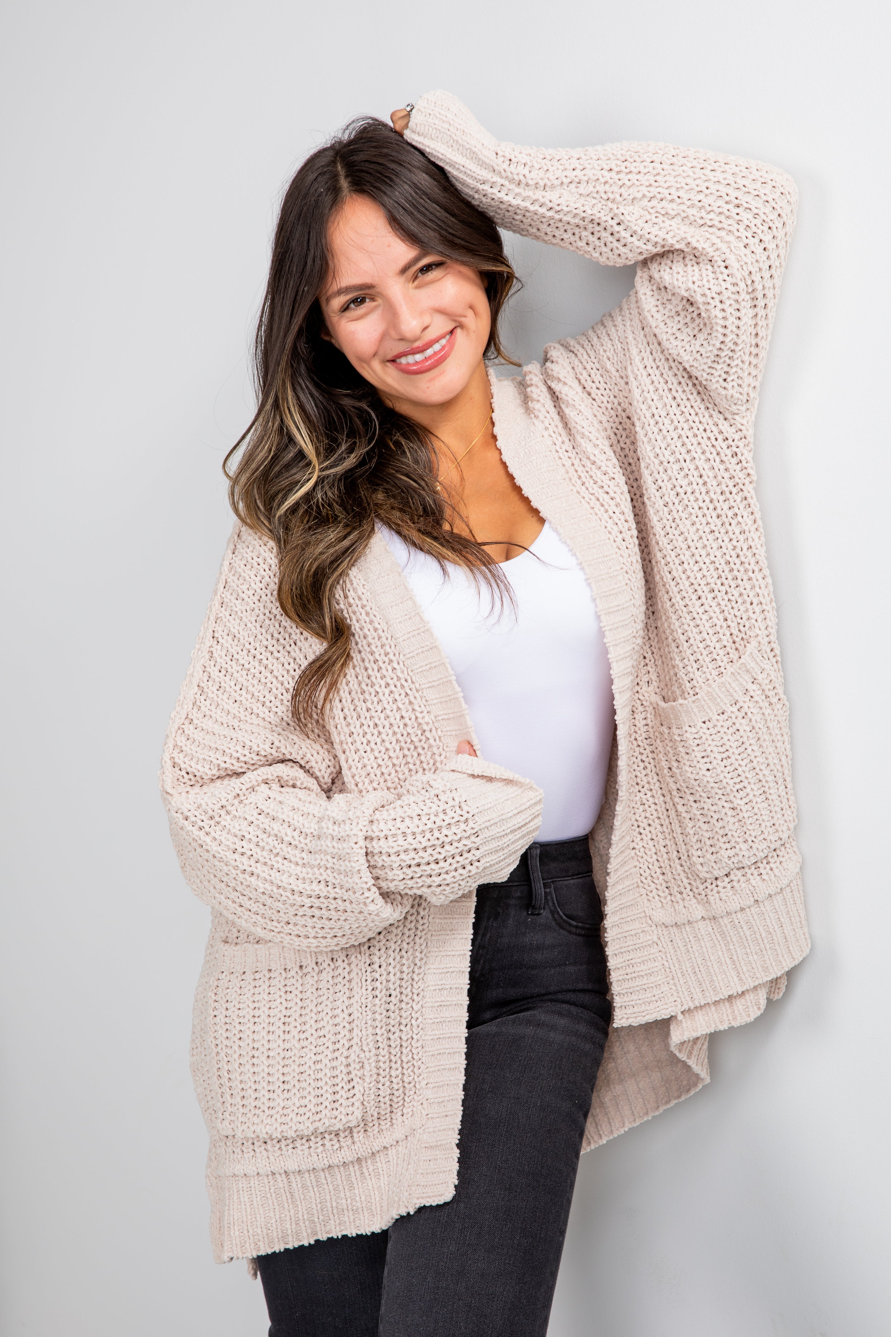 Woman wearing a beige cardigan over a white shirt with black pants on a light gray background