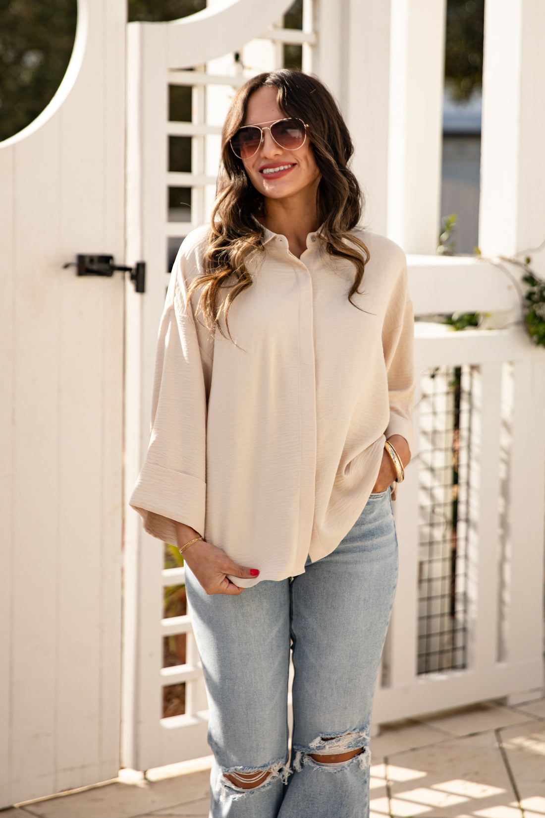 Woman wearing a beige blouse and light blue jeans standing in front of a white wooden door.