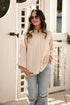 Woman wearing a beige blouse and light blue jeans standing in front of a white wooden door.
