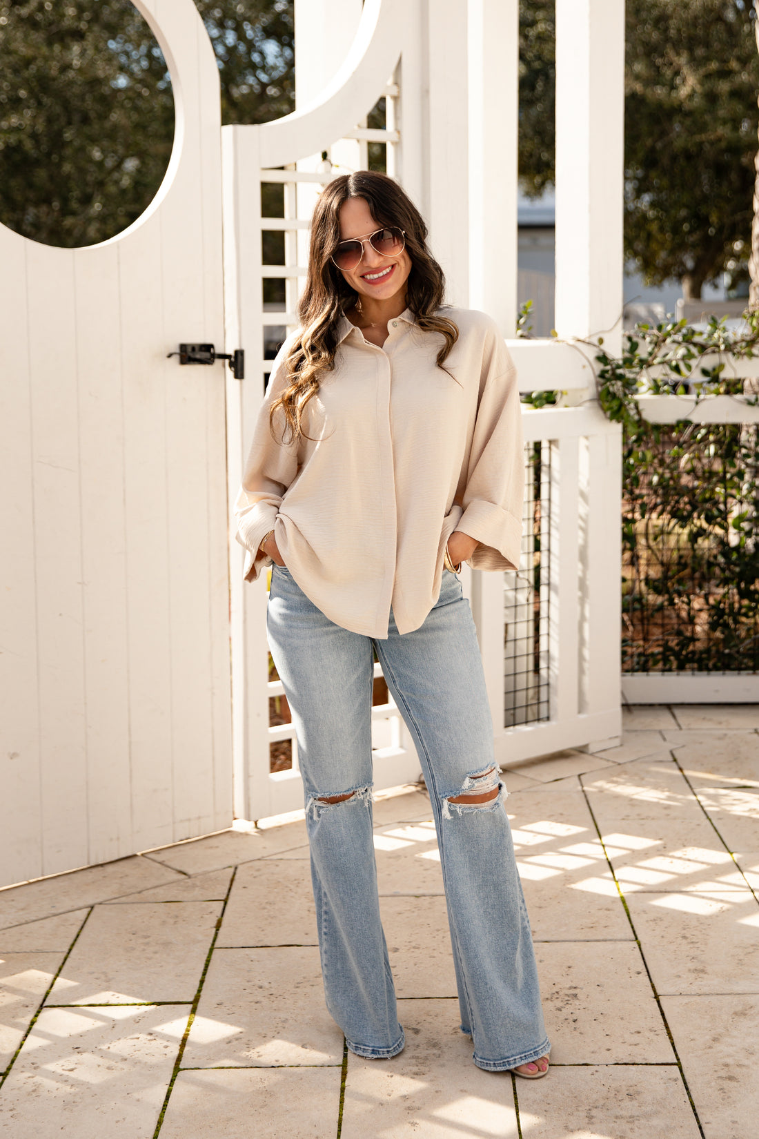 Woman in a beige jacket and light blue jeans standing on a patio.