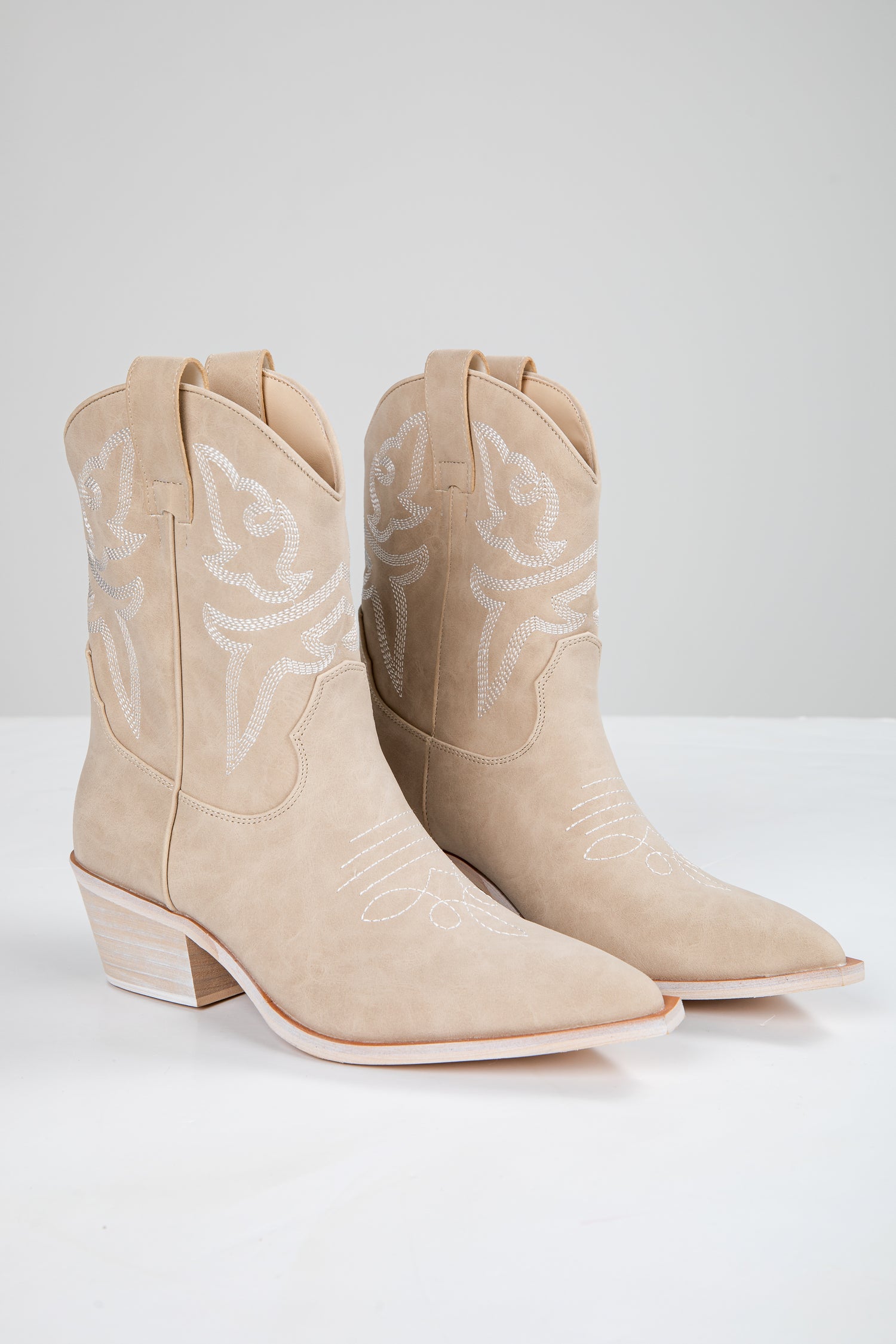 Pair of beige cowboy boots with white embroidery on a white background