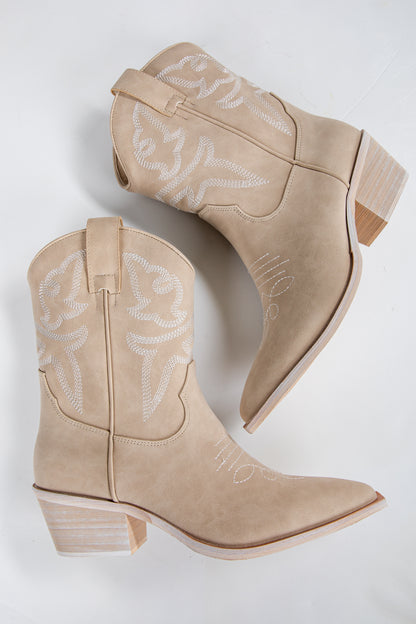 Pair of beige cowboy boots with white embroidery on a light gray background