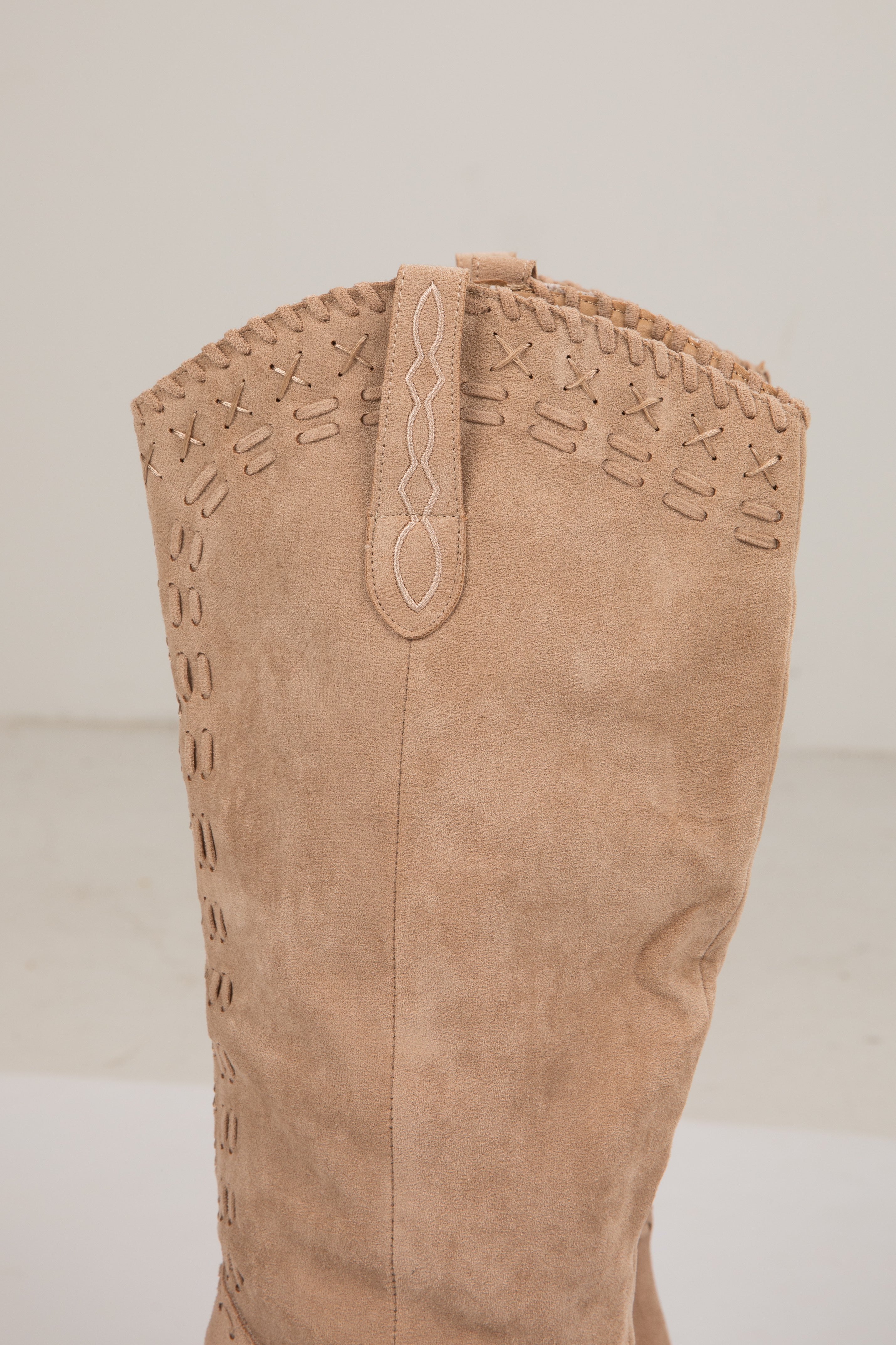 Tan knee-high boot with decorative stitching on a light background