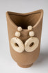 Pair of beige raffia earrings displayed on a textured brown vase.