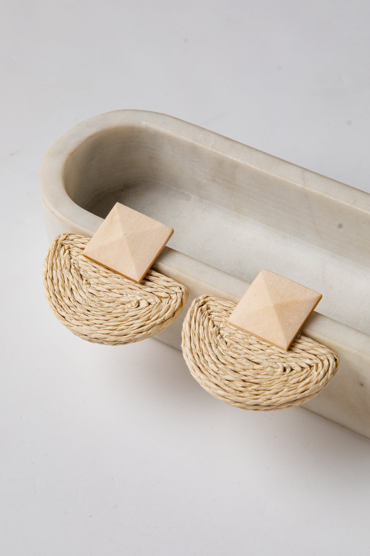 Pair of earrings with woven design on a beige tray against a light background