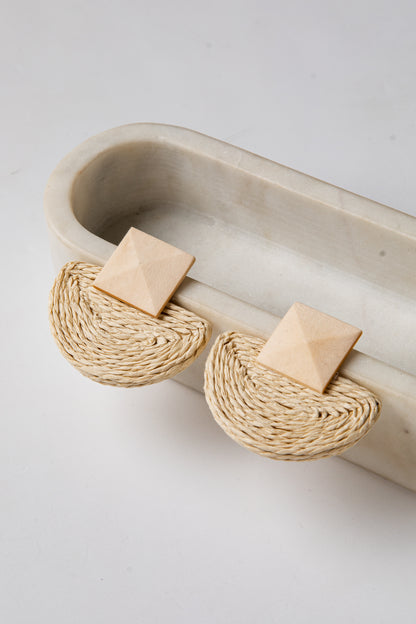 Pair of earrings with woven design on a beige tray against a light background