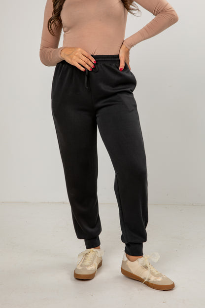 Person wearing black sweatpants and beige shoes on a plain background