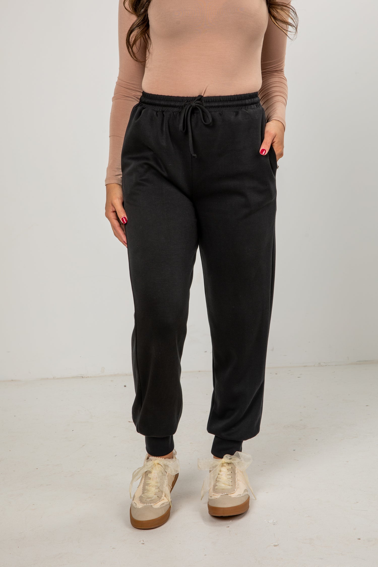 Person wearing black jogger pants and beige sneakers on a white background