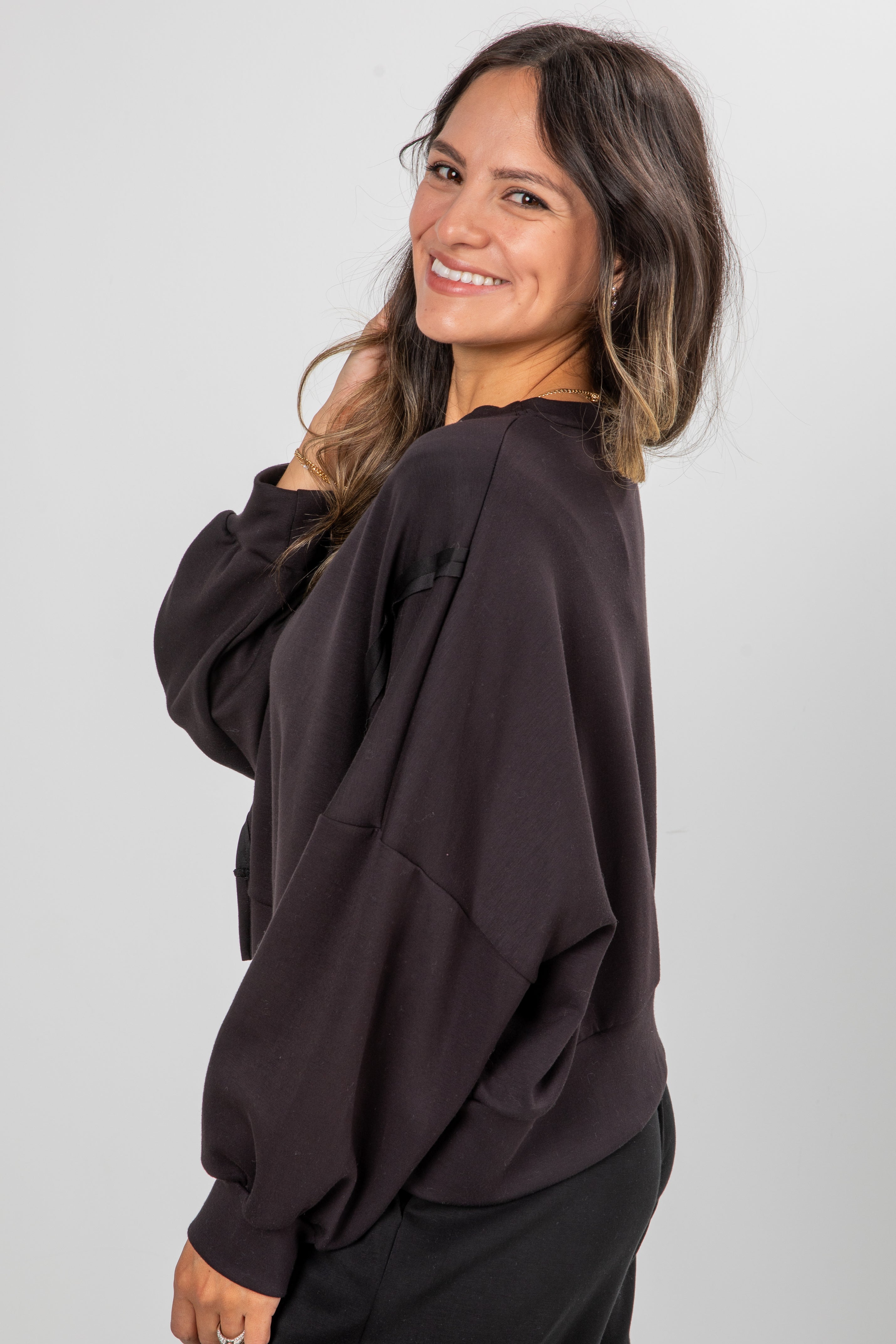 Woman wearing a dark brown oversized sweater against a plain background