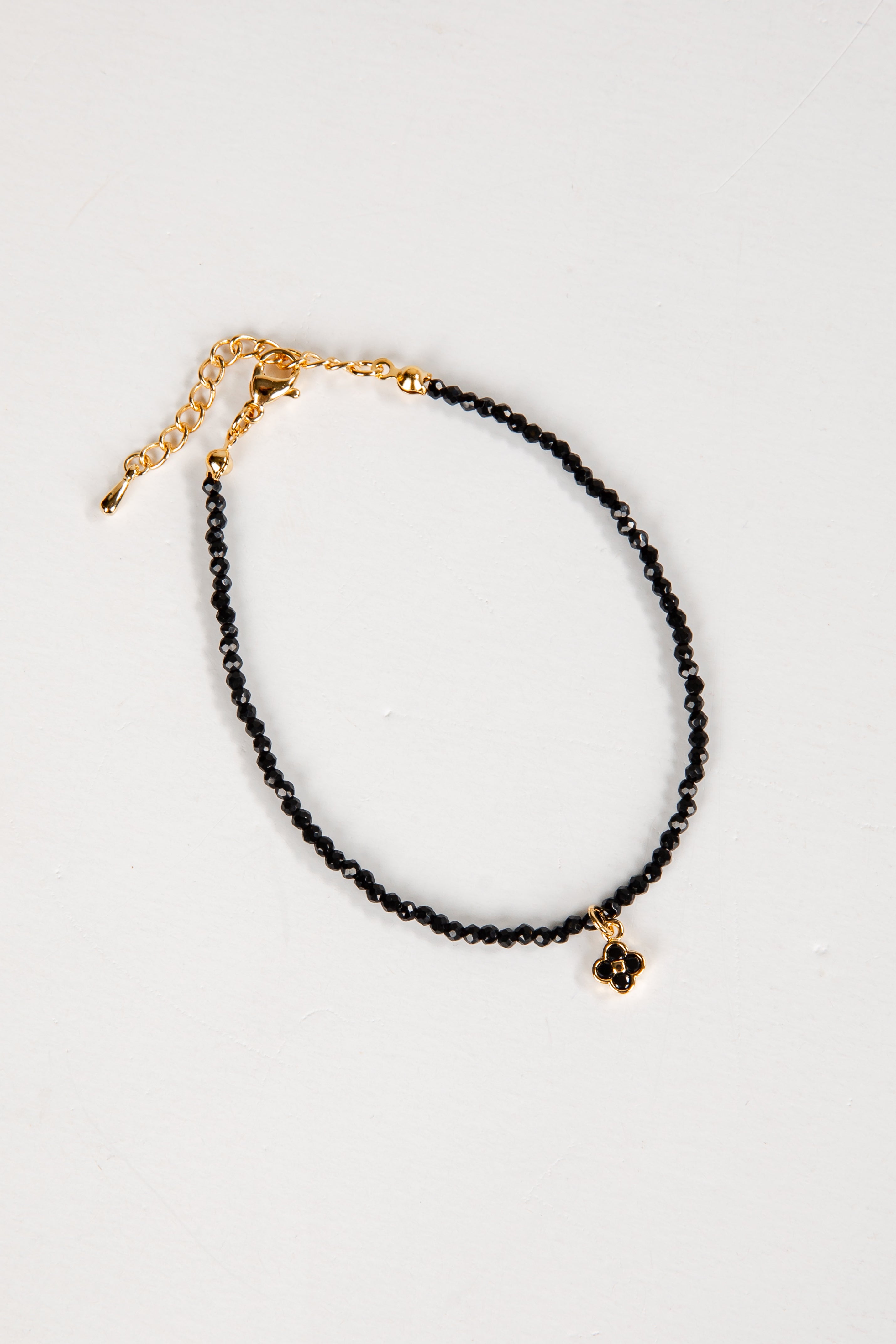 Black beaded anklet with gold chain on a white background