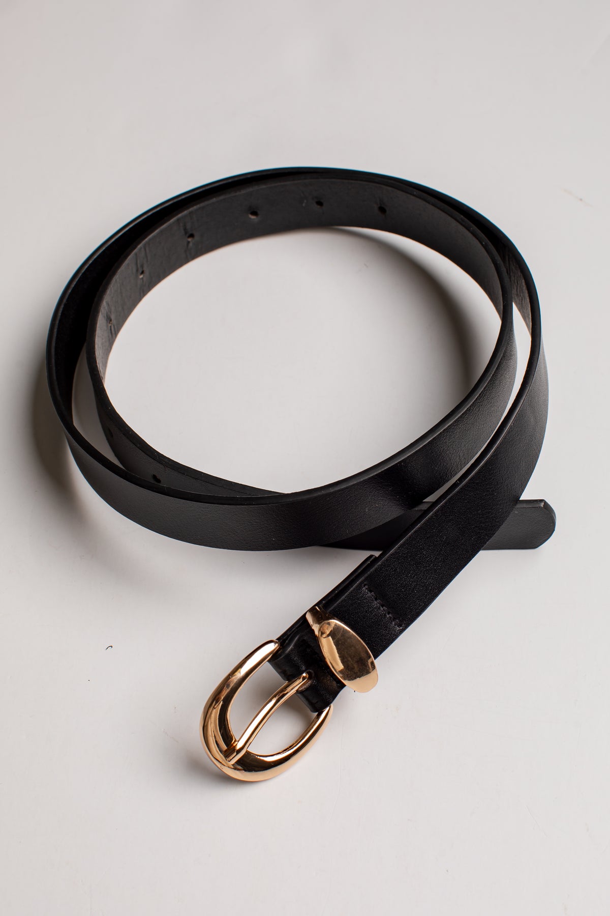 A black leather belt with a polished gold-tone metal buckle, coiled on a light gray background.