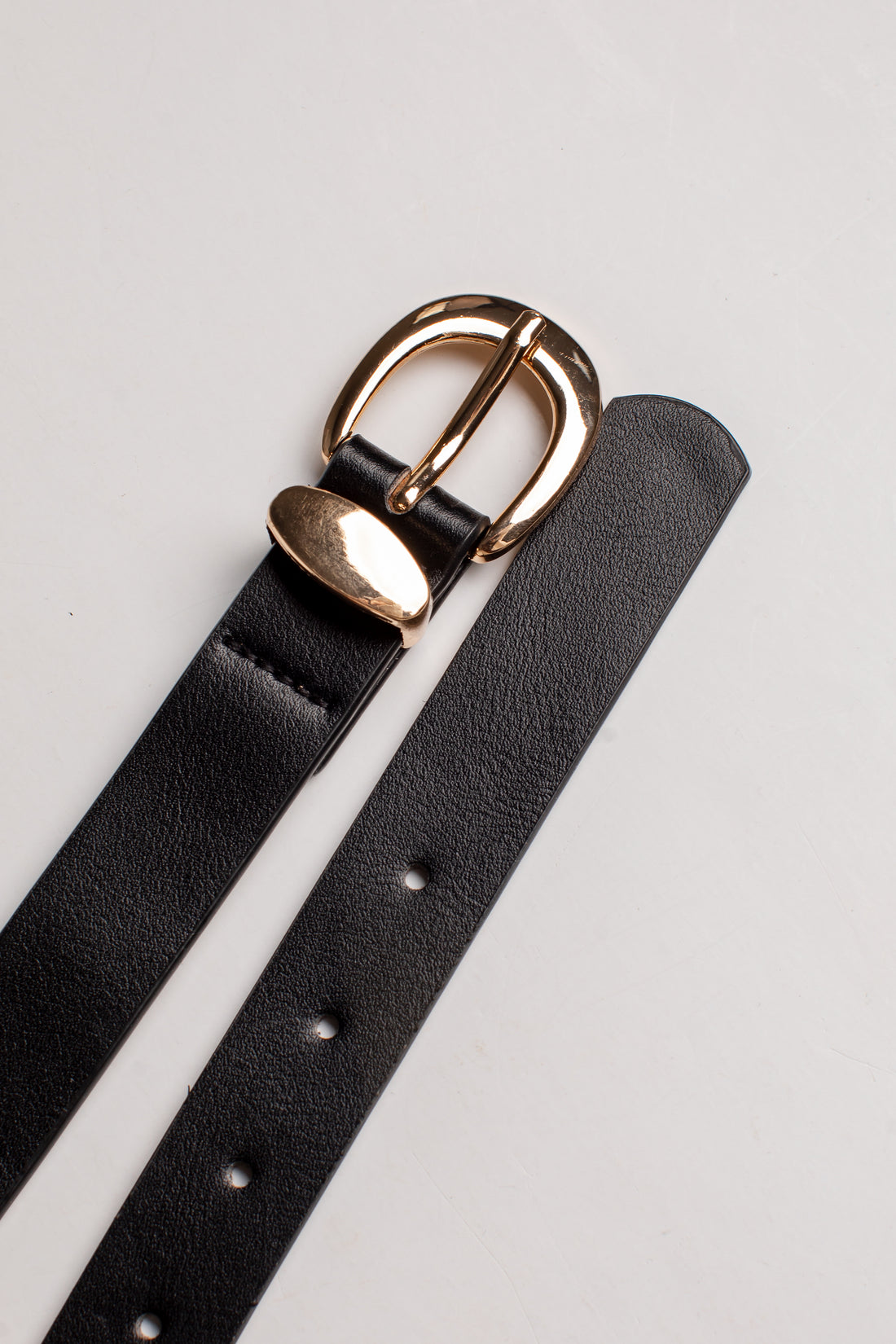A close-up of a black leather belt strap with a polished gold-tone metal buckle, laid diagonally on a light gray background.