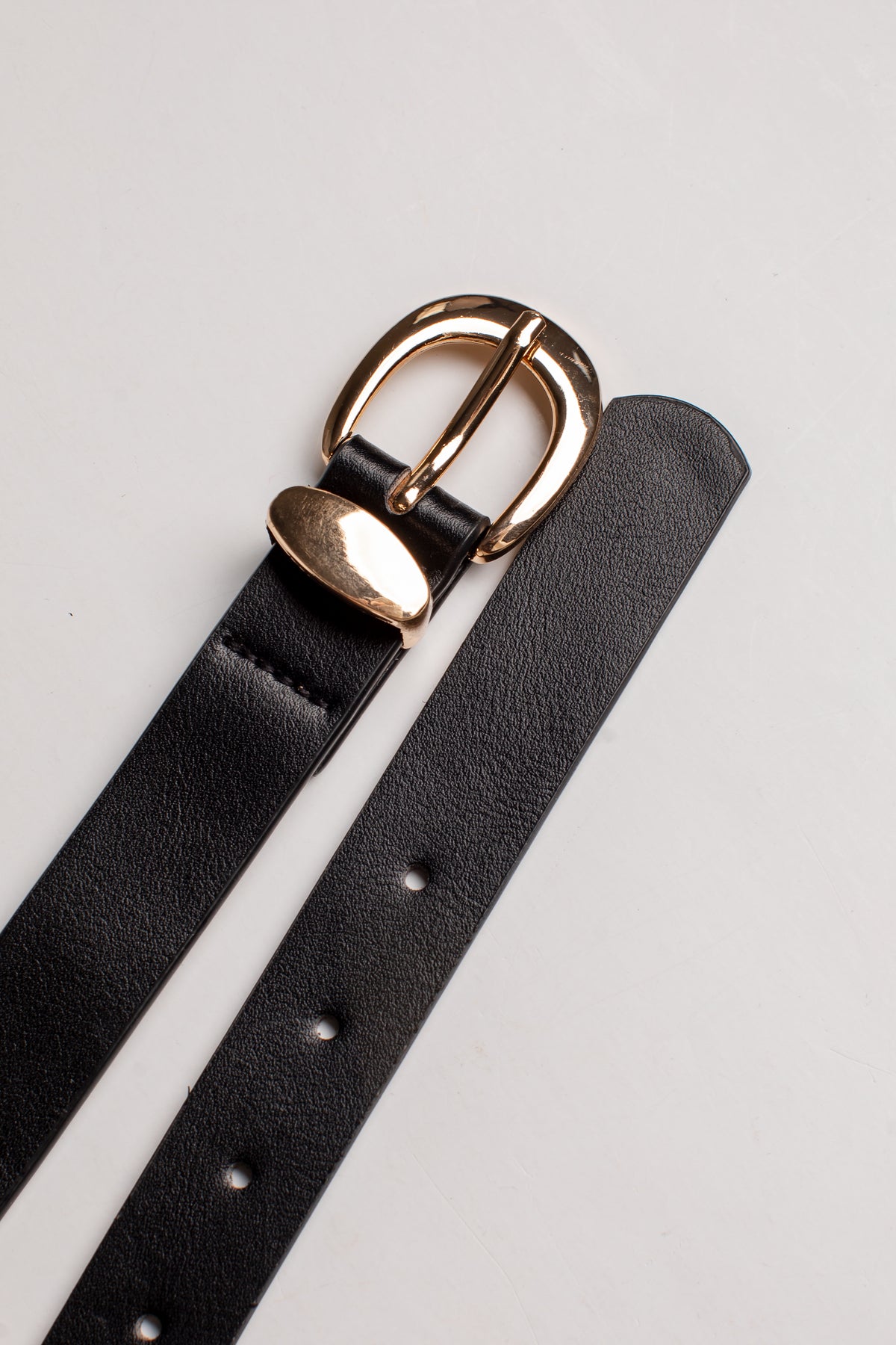 A close-up of a black leather belt strap with a polished gold-tone metal buckle, laid diagonally on a light gray background.