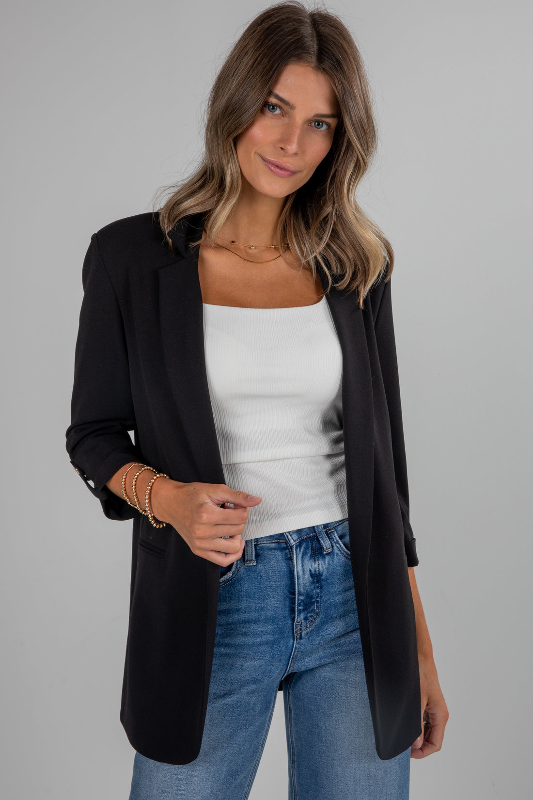 Woman wearing a black blazer, white top, and blue jeans on a gray background