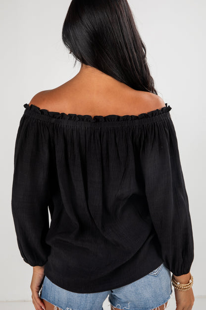 Black off-shoulder top worn by a person on a white background