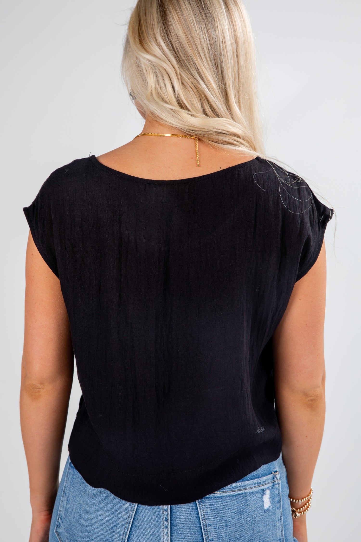 Person wearing a black top and blue jeans on a plain background