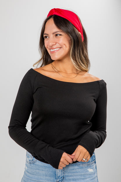 Woman wearing a black off-shoulder top and blue jeans with a red headband against a gray background