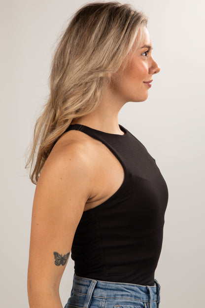 Woman wearing a black tank top and blue jeans against a plain background