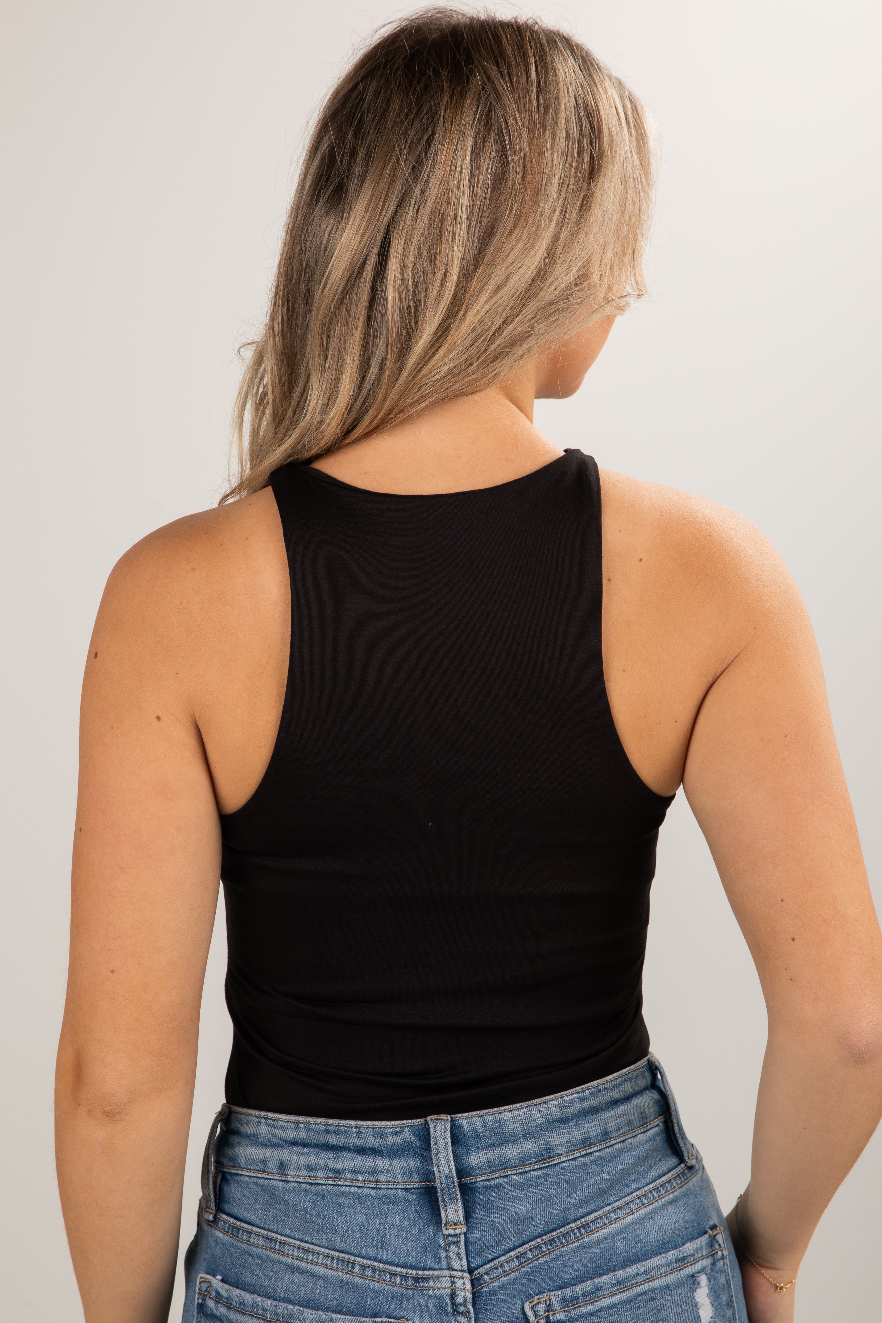Person wearing a black tank top and blue jeans against a plain background