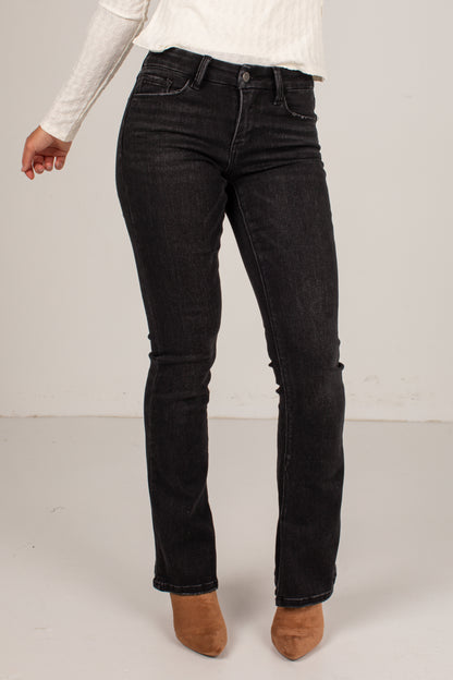A person wearing black denim jeans, a white ribbed long-sleeve top, and brown suede ankle boots, shown from the waist down against a plain light gray studio background.