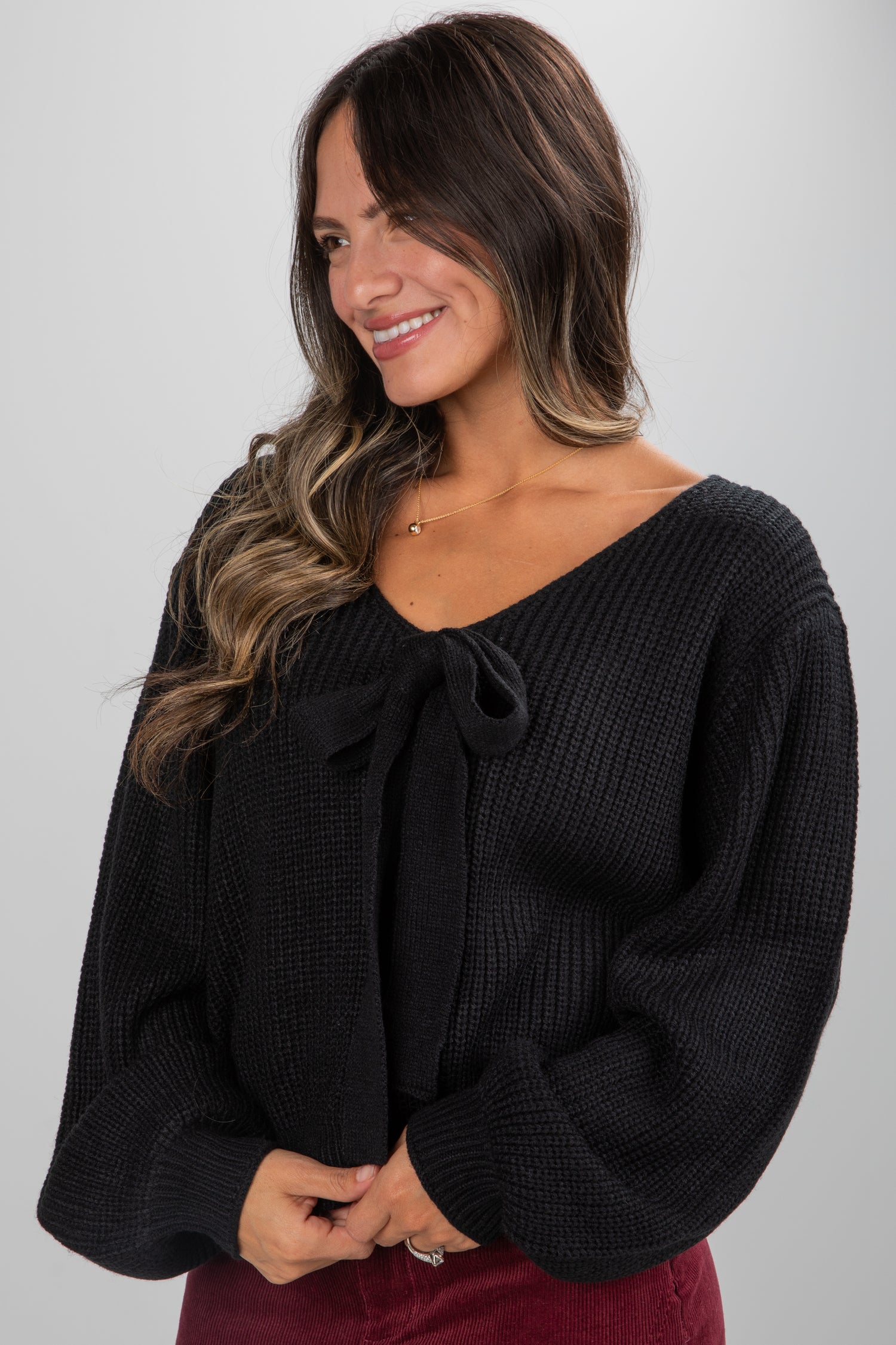Woman wearing a black sweater with a bow detail on a plain background