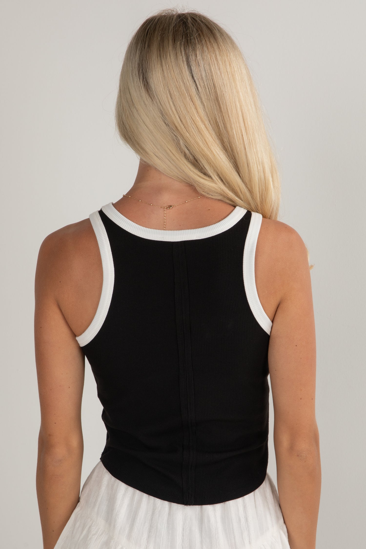 Person wearing a black tank top with white trim on a plain background