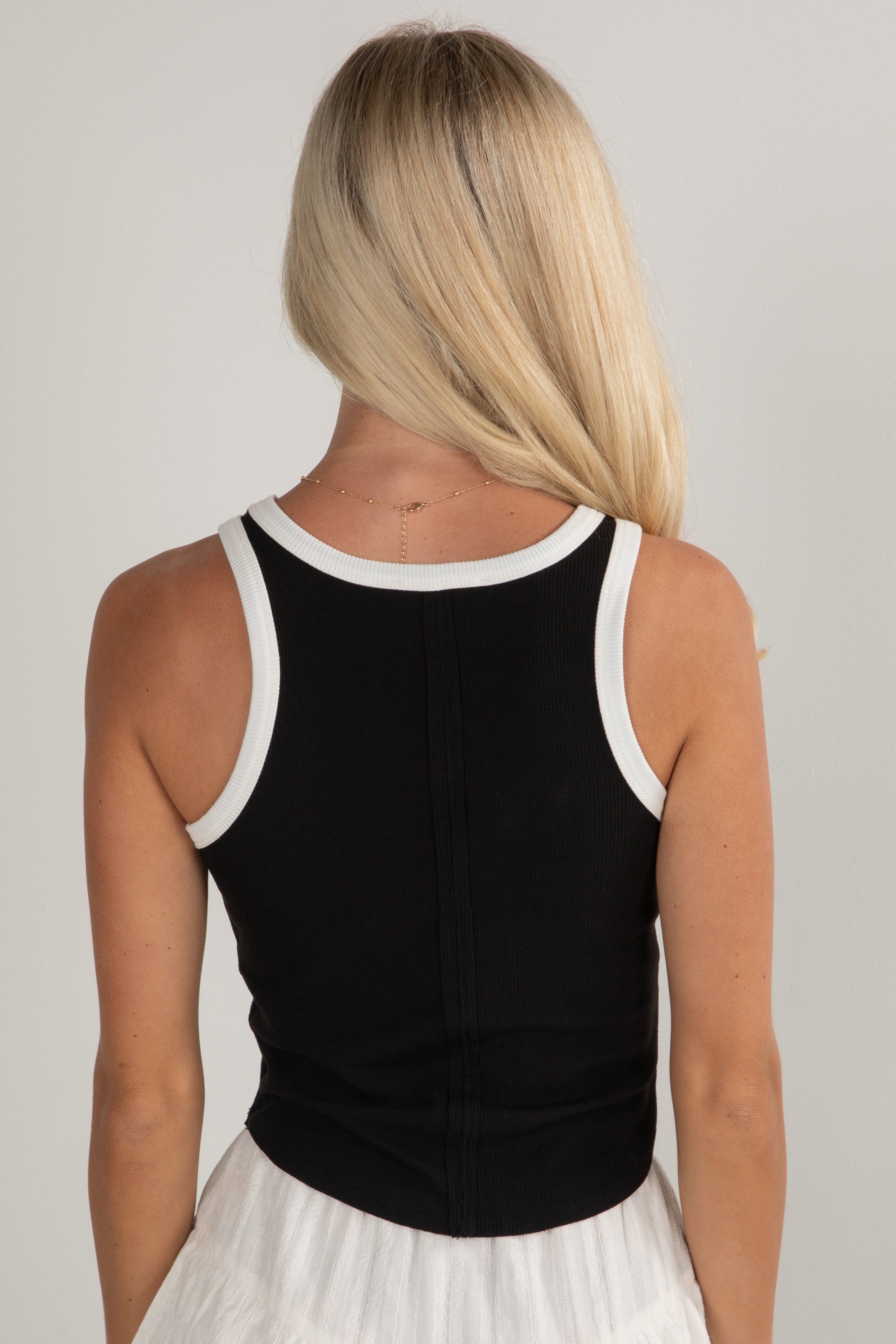 Person wearing a black tank top with white trim on a plain background