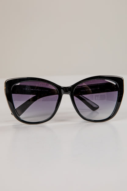 Black cat-eye sunglasses with purple-tinted lenses on a light gray background