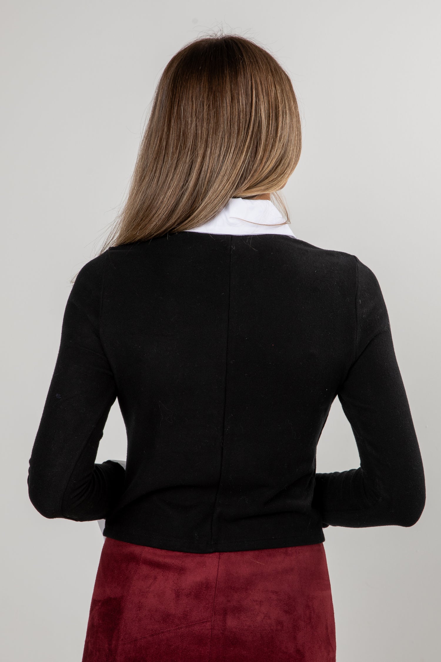 Person wearing a black cardigan over a white shirt with a red skirt on a plain background