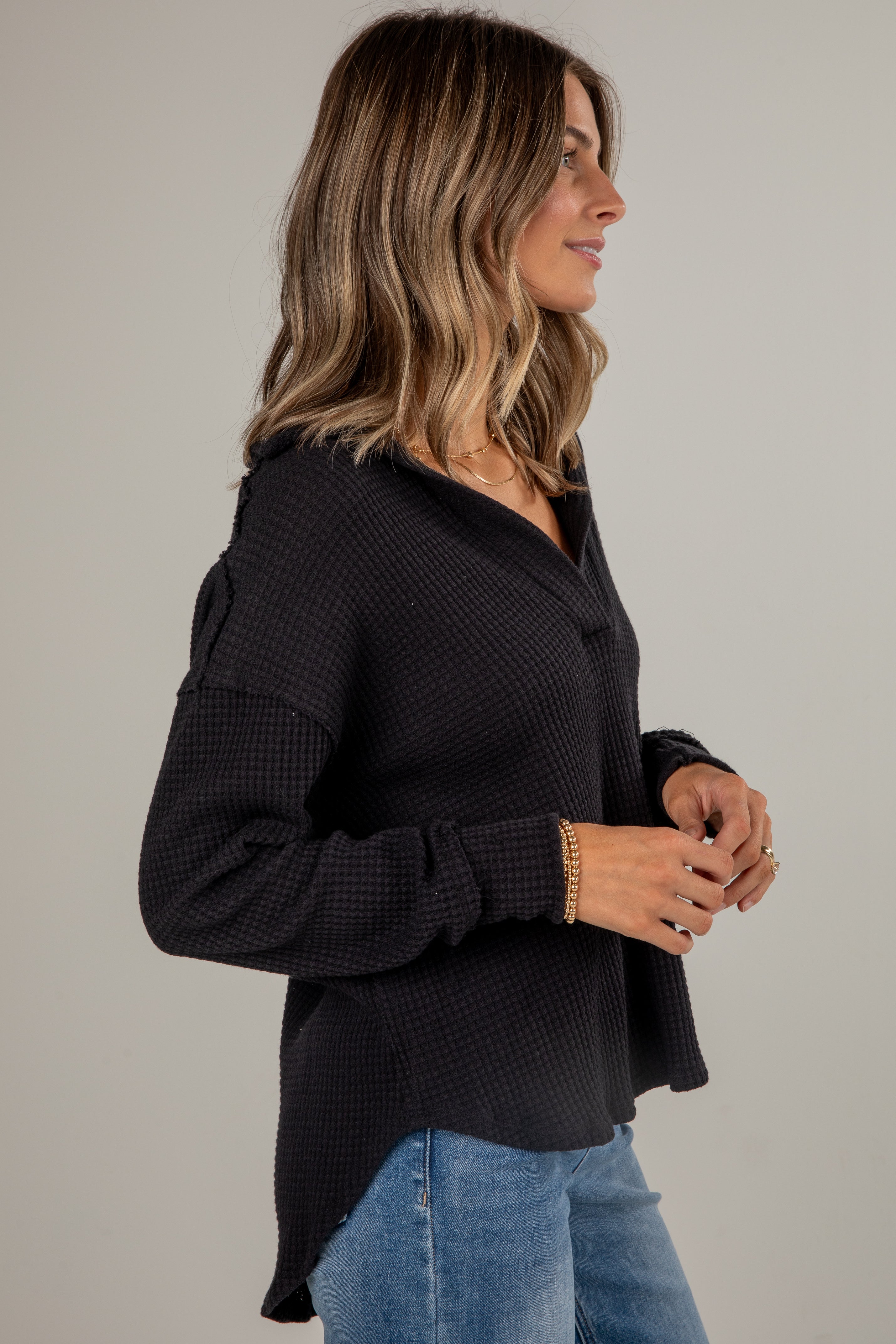 Woman wearing a black textured sweater and blue jeans against a plain background