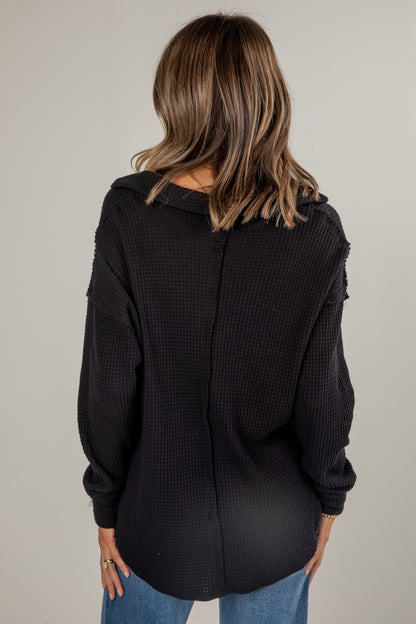 Person wearing a black textured sweater with a neutral background