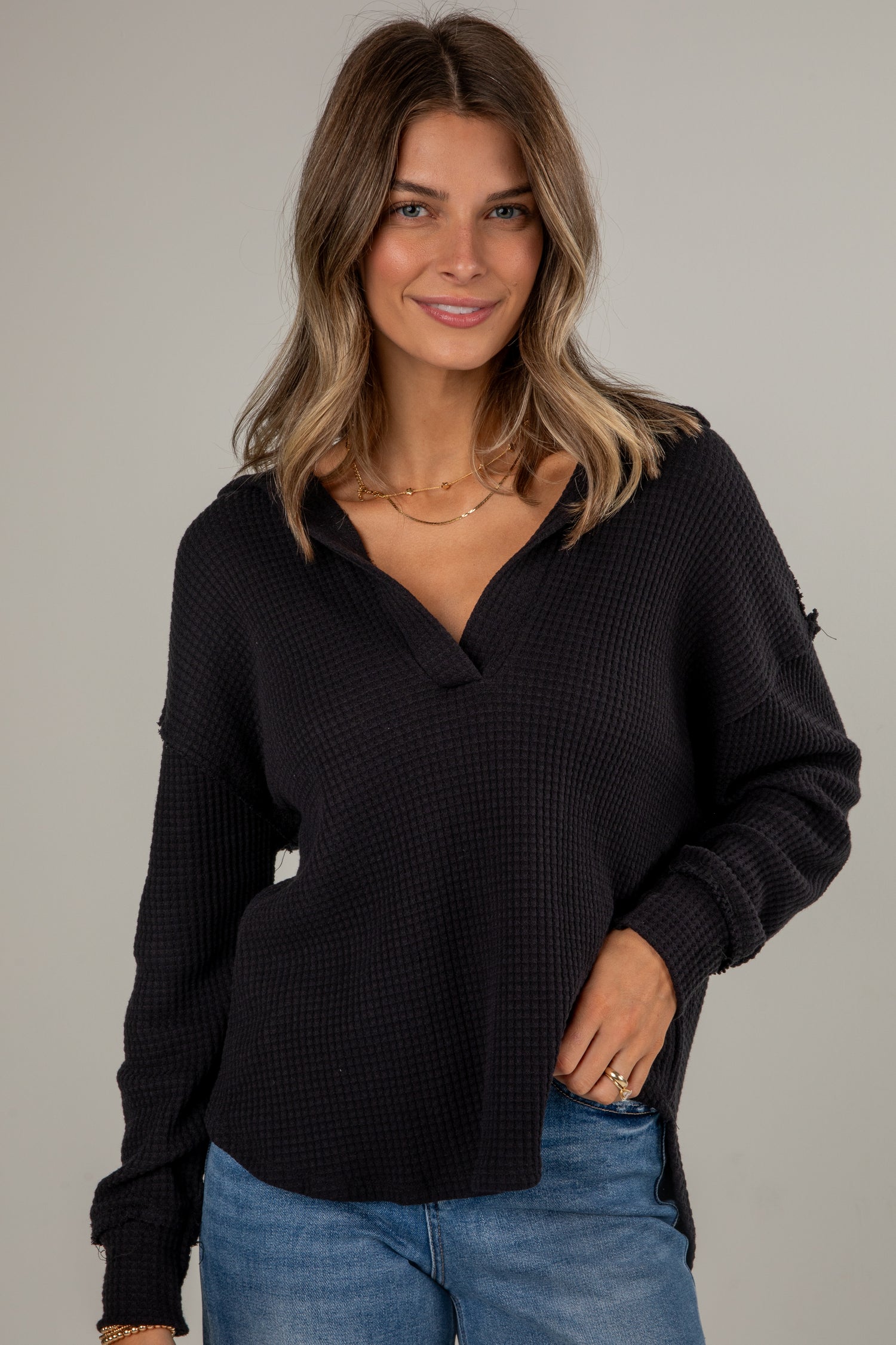 Woman wearing a black sweater and blue jeans against a neutral background
