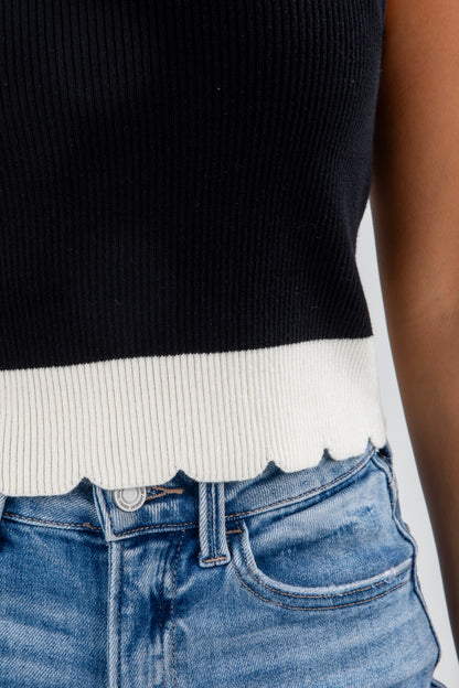 Person wearing a black and white ribbed sweater with blue jeans on a light gray background