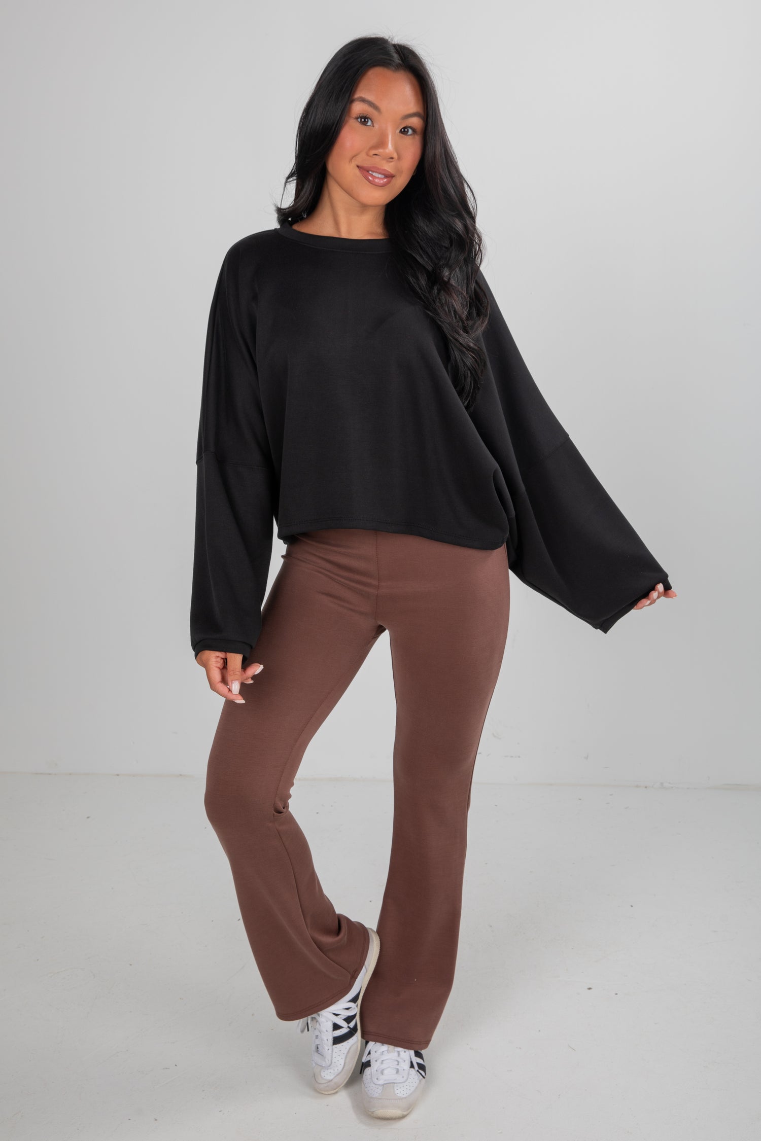 Woman wearing a black top and brown pants on a white background