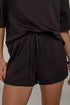 A close-up of a person wearing dark black drawstring shorts and a matching dark top, cropped from the chest to the upper thighs against a plain light background.
