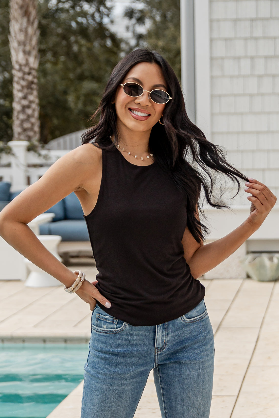 Woman wearing a black tank top and blue jeans by a poolside.