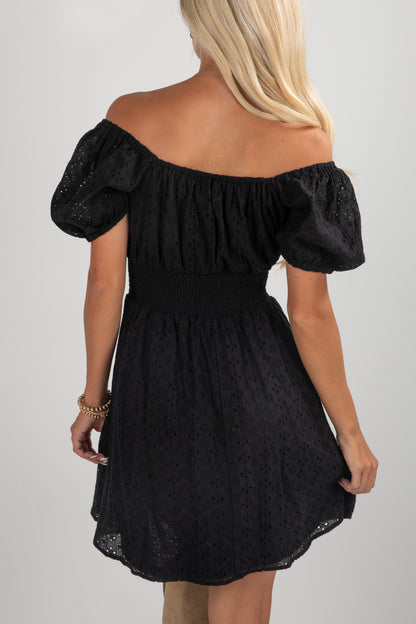Black off-shoulder dress worn by a person on a plain background