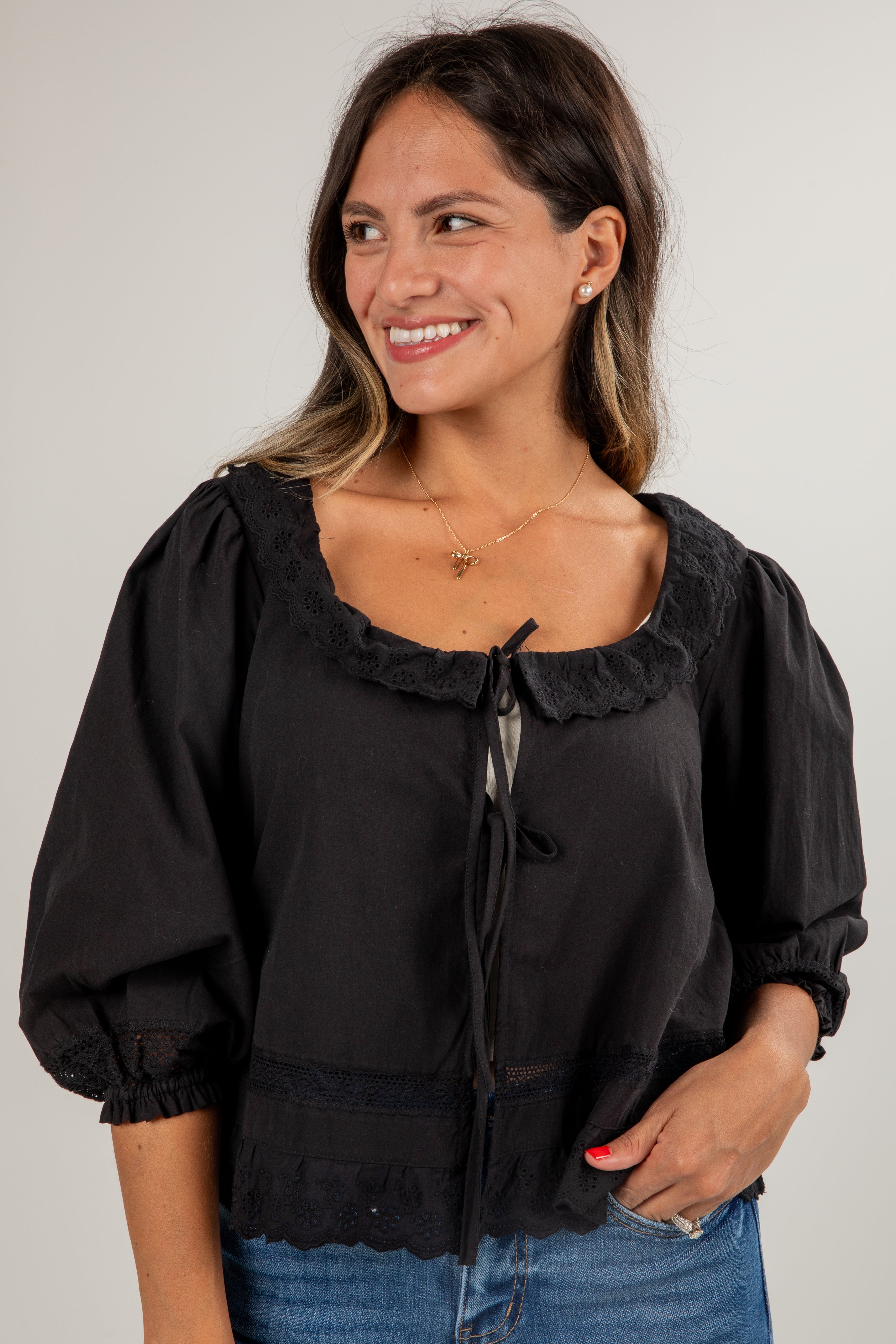 Woman wearing a black blouse with ruffled collar and cuffs against a plain background